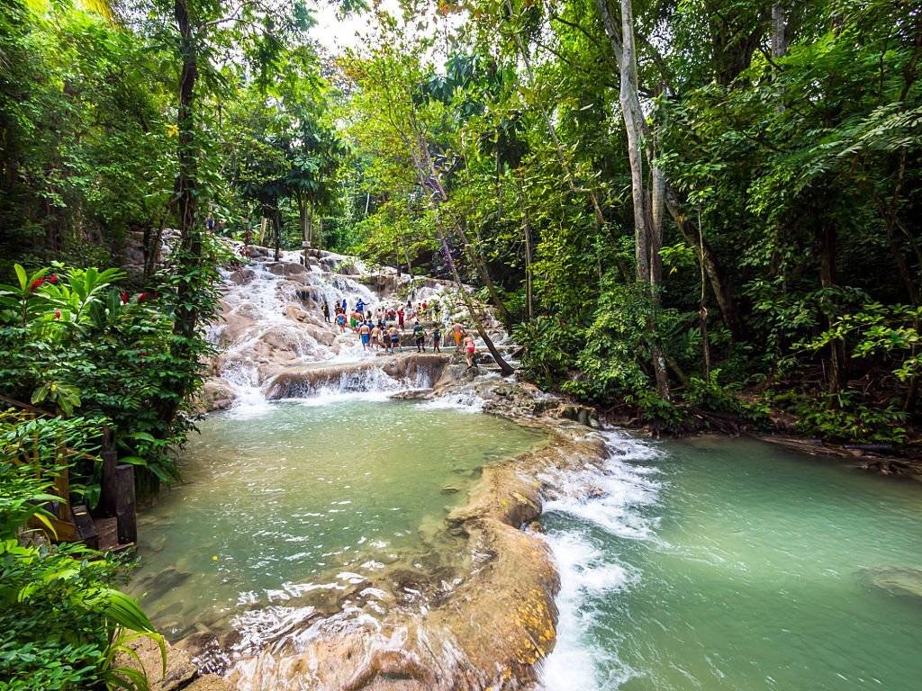 "Dunn's River Falls, Jamaica: A majestic waterfall surrounded by lush greenery, with visitors climbing the cascading rocks."